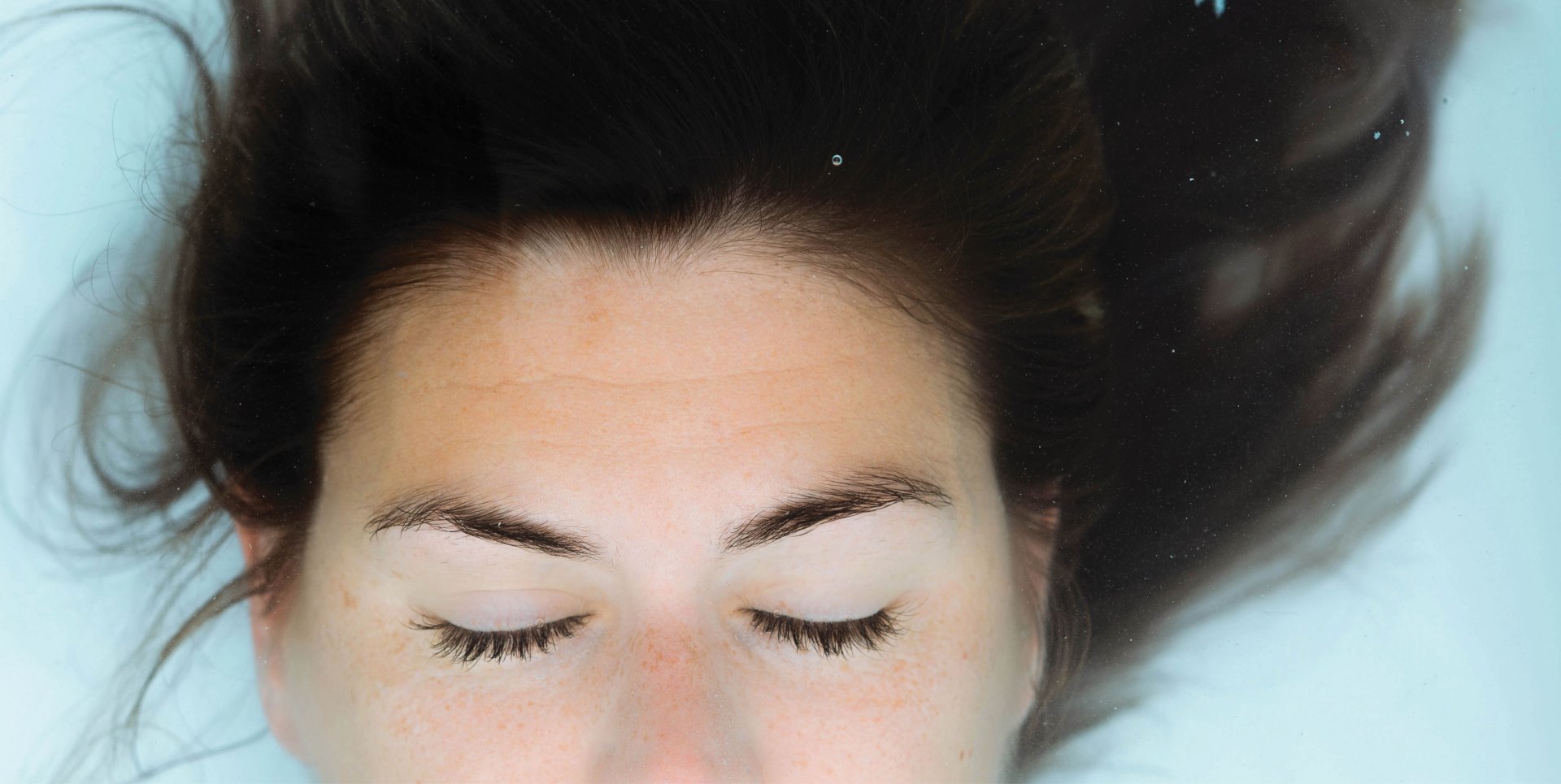 close-up portrait of a woman's face submerged in water, with a serene expression and closed eyes