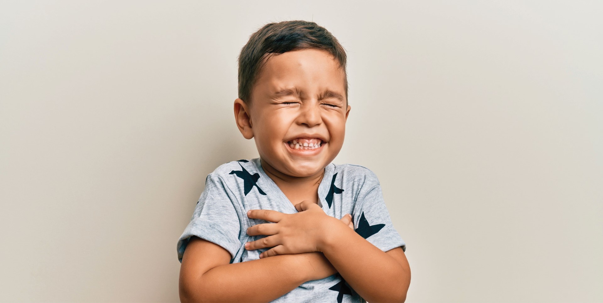 young boy laughing heartily and clutching his chest with his eyes closed after a good night's sleep