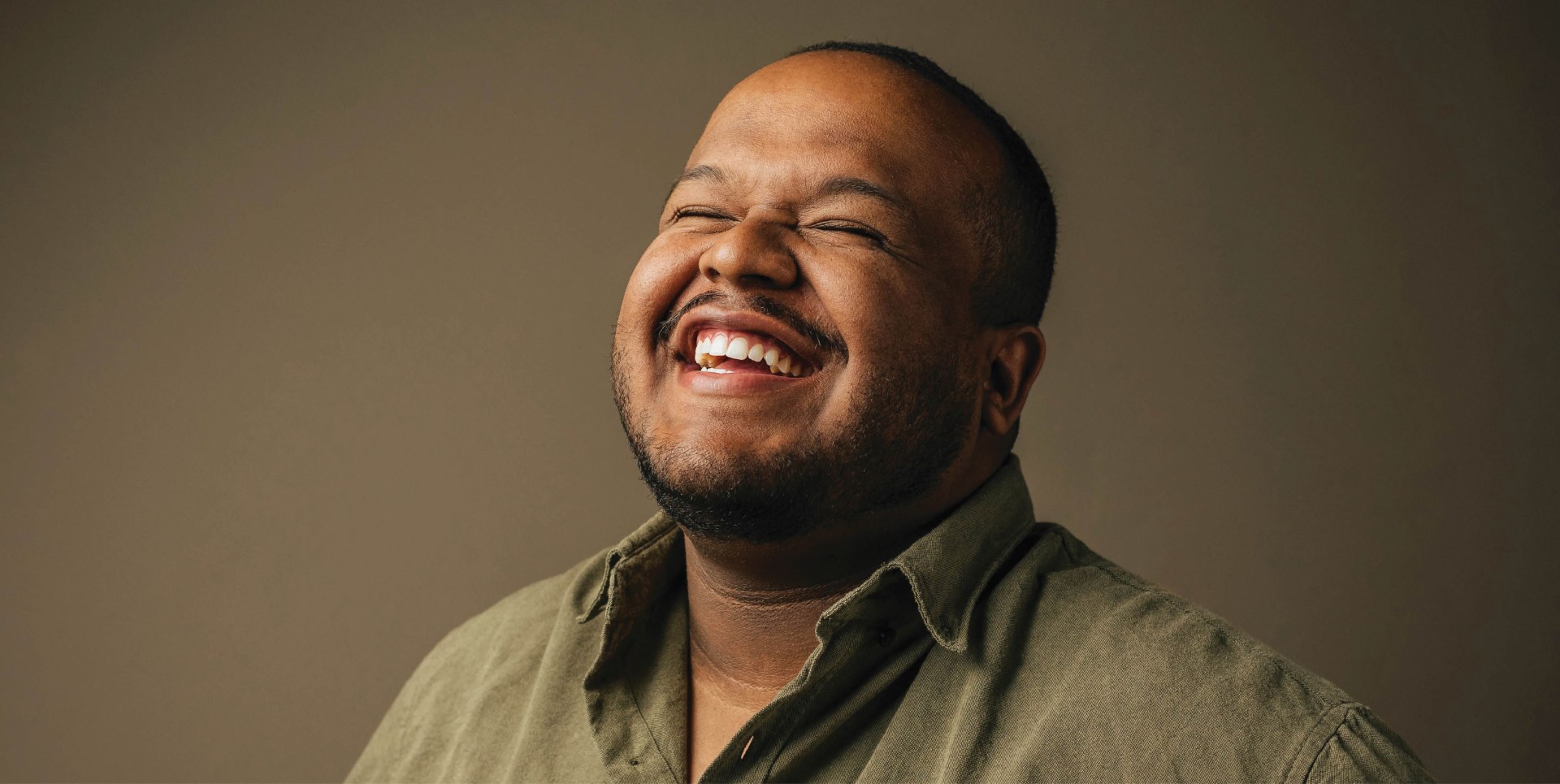 Joyous middle-aged man in a green shirt laughing heartily with closed eyes