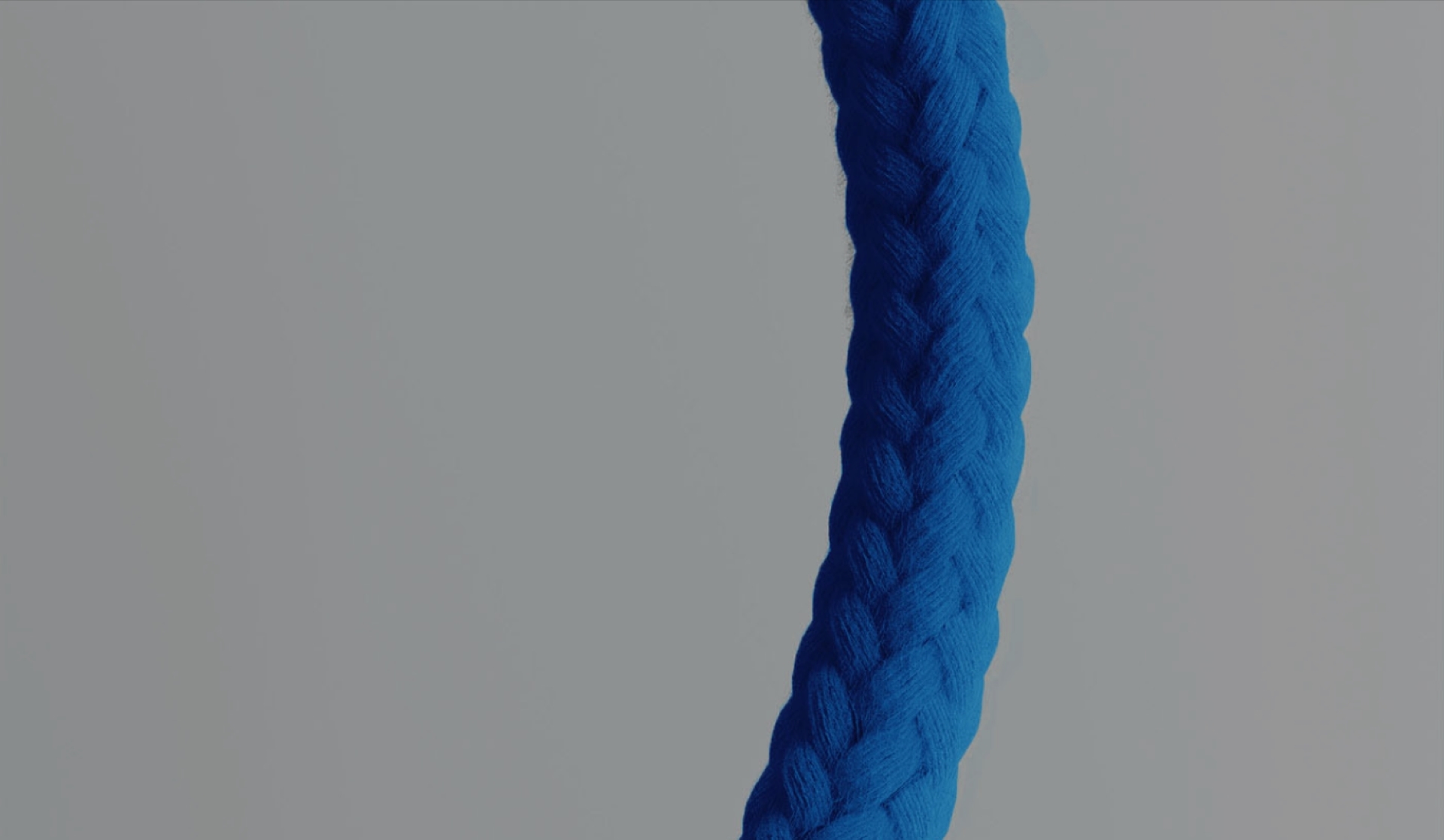 Close-up of a blue braided yarn thread against a gray background, highlighting its intricate texture.