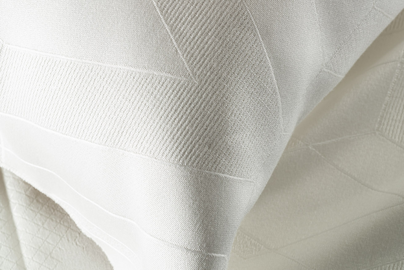 A piece of white mattress and pillow featuring a creamy fabric with an intricate geometric pattern